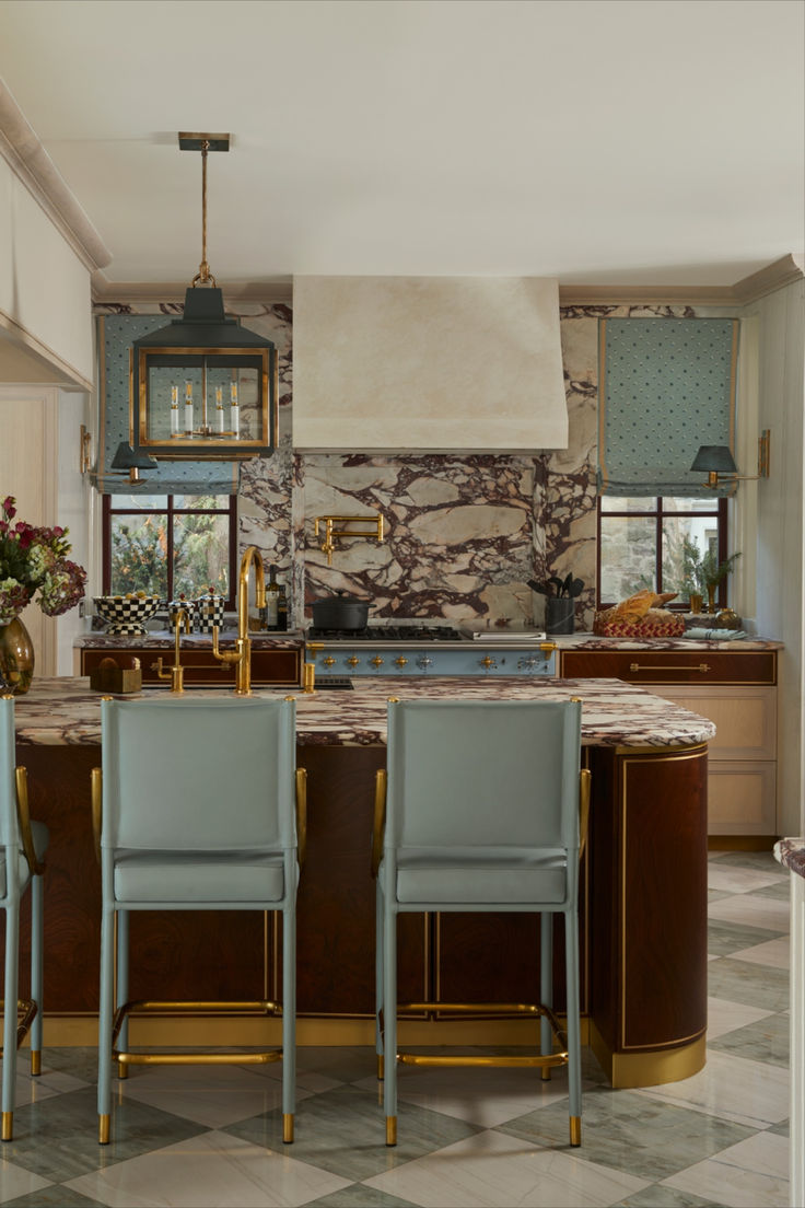 a kitchen with marble counter tops and blue chairs in front of an island that has gold trim