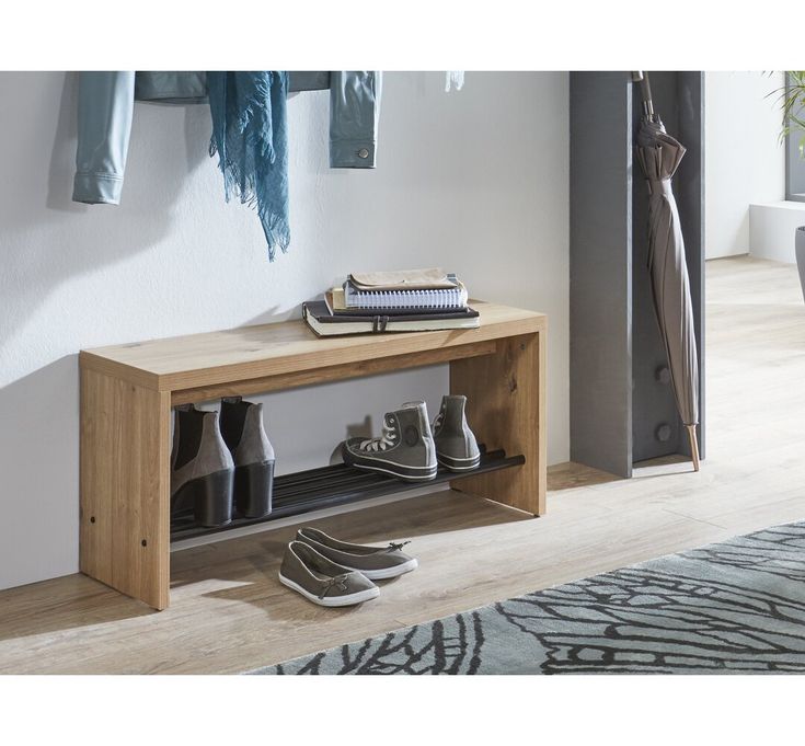 a wooden bench with shoes on it in front of a wall mounted coat rack and clothes