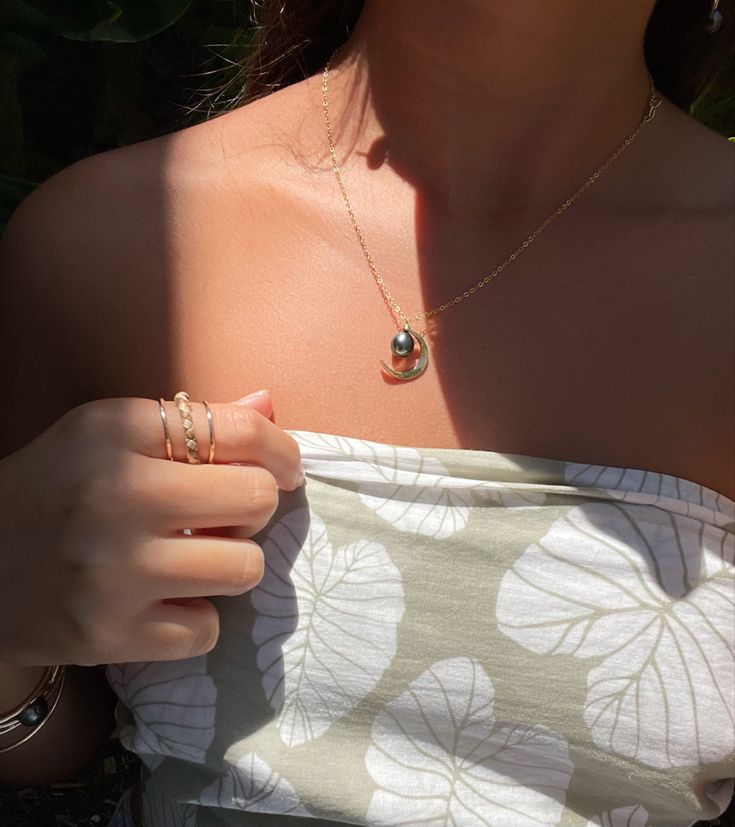 a woman in a white dress holding onto her gold ring and necklace with a flower pattern on it