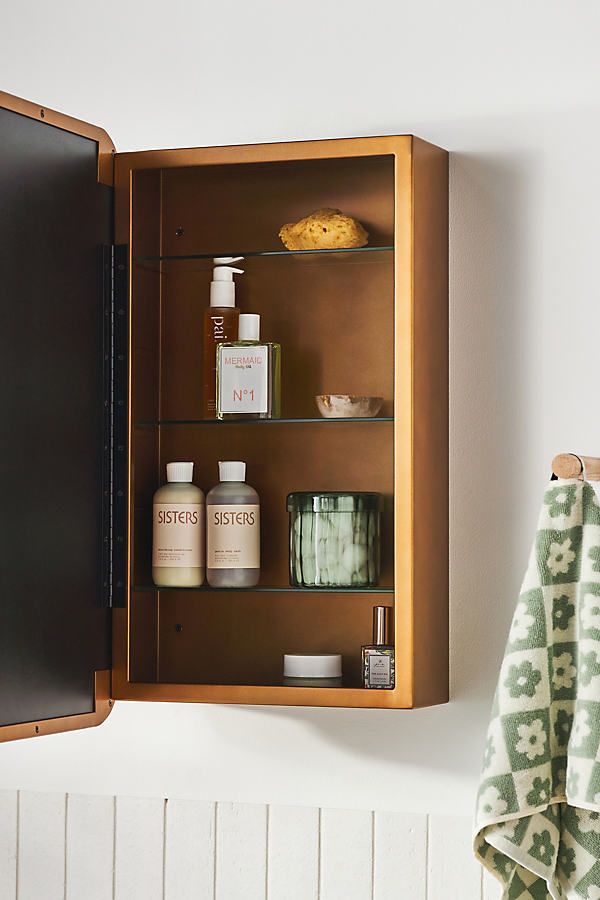 a wooden medicine cabinet with bottles and soaps on the top shelf next to a towel