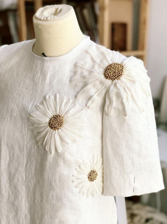 a white dress with flowers on the front and back, sitting on a mannequin