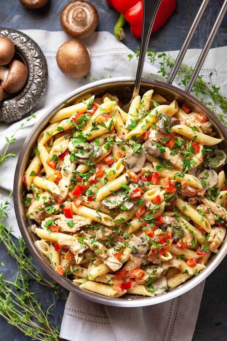 a pan filled with pasta and vegetables on top of a table next to mushrooms, peppers, and parsley