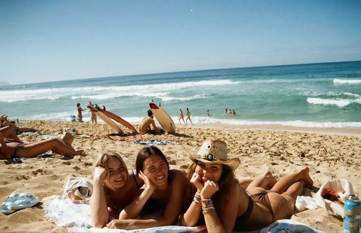 two women laying on the beach with their arms around each other and smiling at the camera