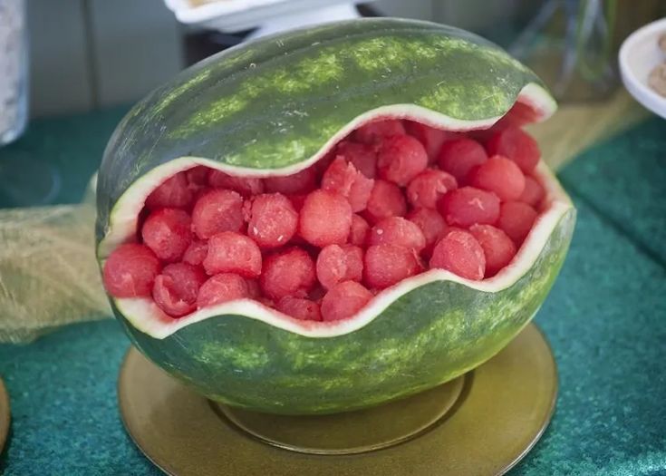 a watermelon filled with red berries on top of a green table cloth and gold plate