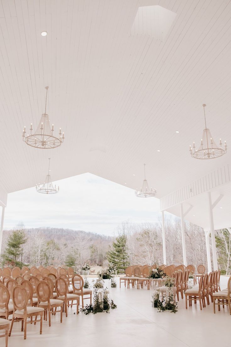 an indoor wedding venue with rows of wooden chairs and chandeliers on the ceiling