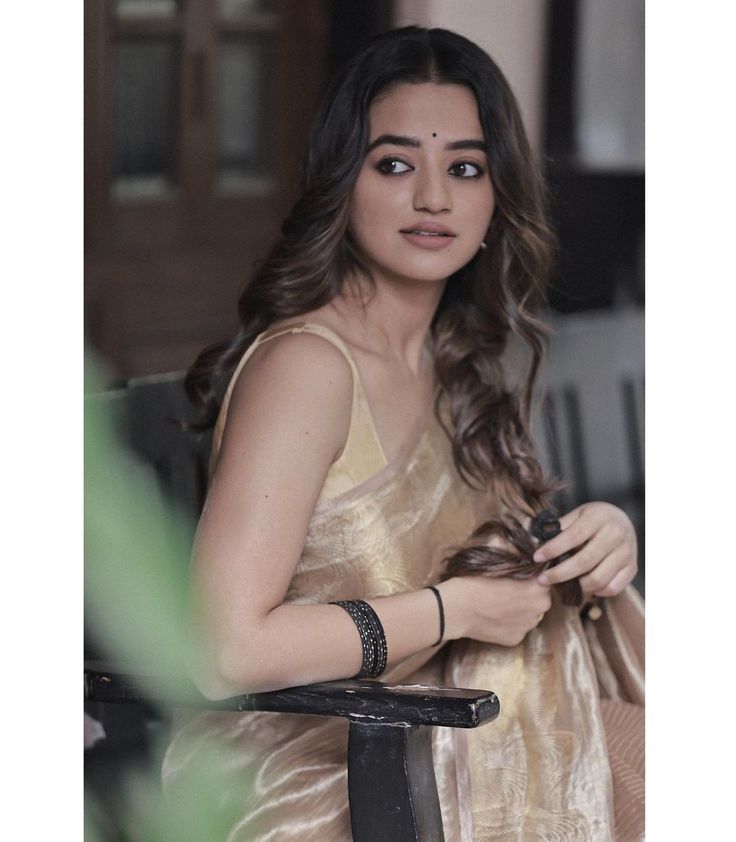 a beautiful young woman sitting in a chair looking at her cell phone while wearing a gold sari