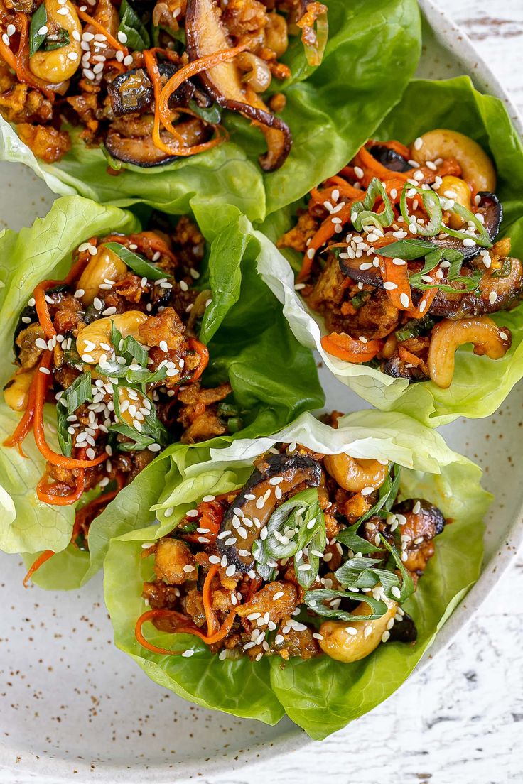 four lettuce wraps filled with meat and veggies on a white plate