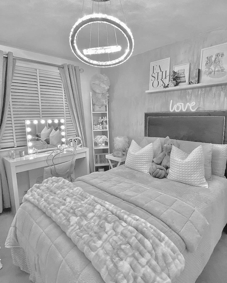 black and white photograph of a bedroom with bed, desk, mirror and lights hanging from the ceiling