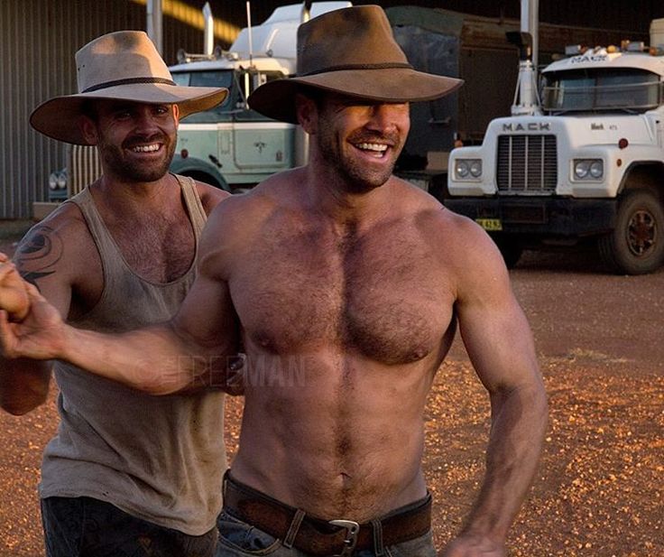 two shirtless men standing next to each other in front of trucks and dirt ground