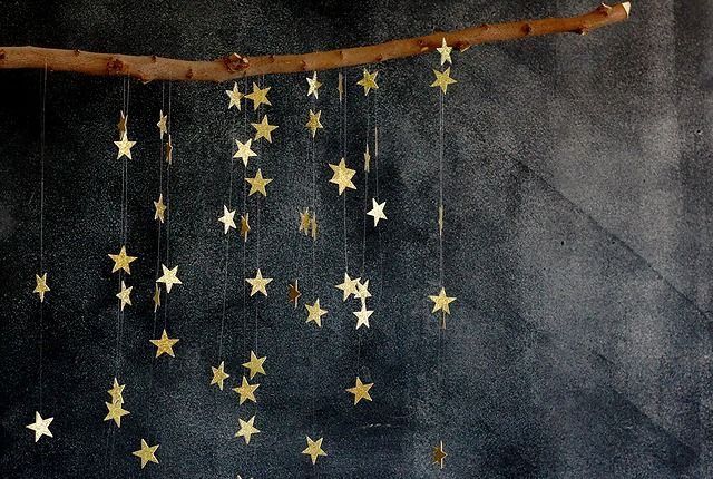 a branch with gold stars hanging from it's sides against a dark background,