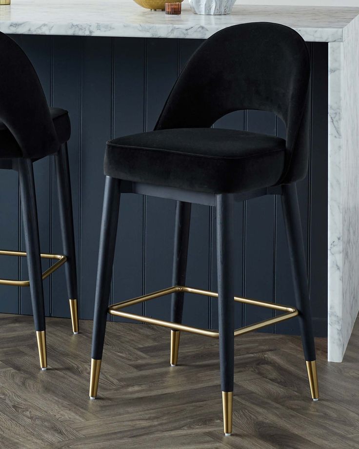 two black velvet bar stools in front of a marble kitchen island with gold legs