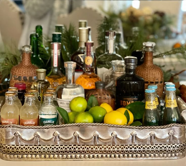 there are many bottles and glasses in the tray on the table with lemons, limes, and other drinks