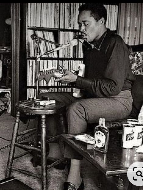 a man sitting on a chair in front of a book shelf filled with books and drinks