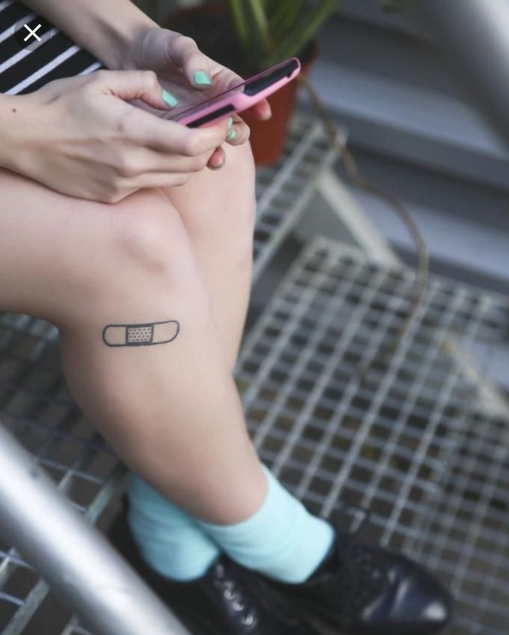 a woman with a small tattoo on her leg is sitting and looking at her cell phone