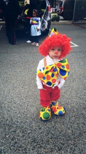 a toddler dressed as a clown standing in the street