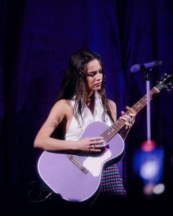 a woman holding a purple guitar in front of a microphone