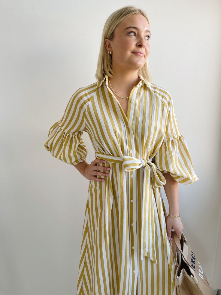 The Ischia Stripe Dress is a shirt dress with flair. Featuring a button down front, shirt collar, tie belt and drop shoulder to an oversized bubble sleeve and pockets. Pair with white tennis shoes or a pair of nude sandals to complete a perfect summer look. Fit: True to sizeFabric Content: 80% Rayon 20% NylonFabric Care: Machine Wash Cold Gentle Cycle, lay flat to dryMeasurements: 45" Shoulder to hemLining: NoZipper: No S:0-2 M:4-6 L:8-10 Yellow Striped Dress, White Tennis Shoes, Nude Sandals, York Dress, Bubble Sleeve, Mother Denim, Stripe Dress, Summer Look, Yellow Stripes