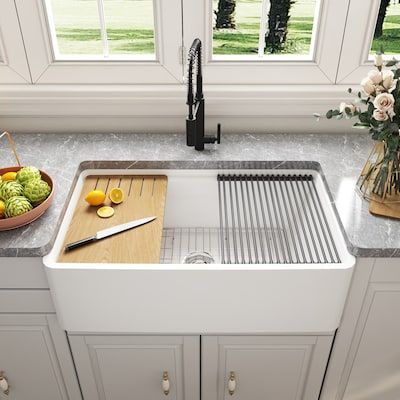 a kitchen sink with cutting board, knife and bowl of fruit on the counter top