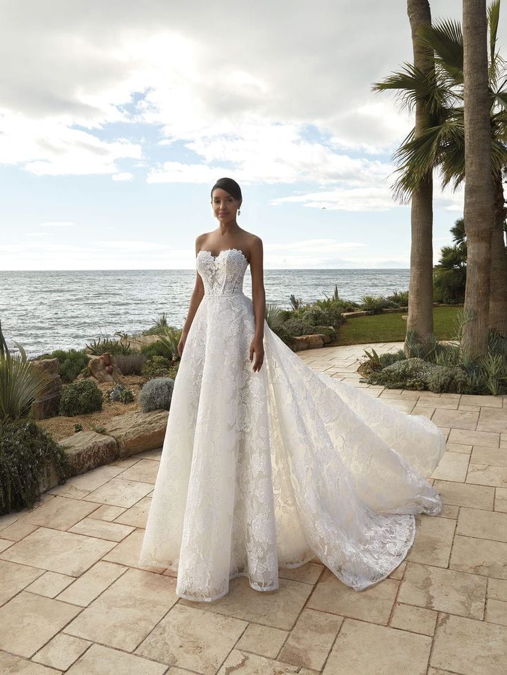 a woman in a white wedding dress standing on a patio near the ocean with palm trees