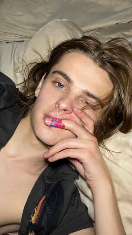 a young man laying on top of a bed with his hand under his mouth and tongue sticking out