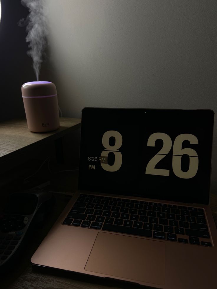 an open laptop computer sitting on top of a wooden desk next to a lamp and clock