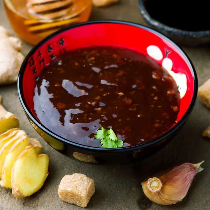 a red bowl filled with sauce next to garlic and other foods on a counter top