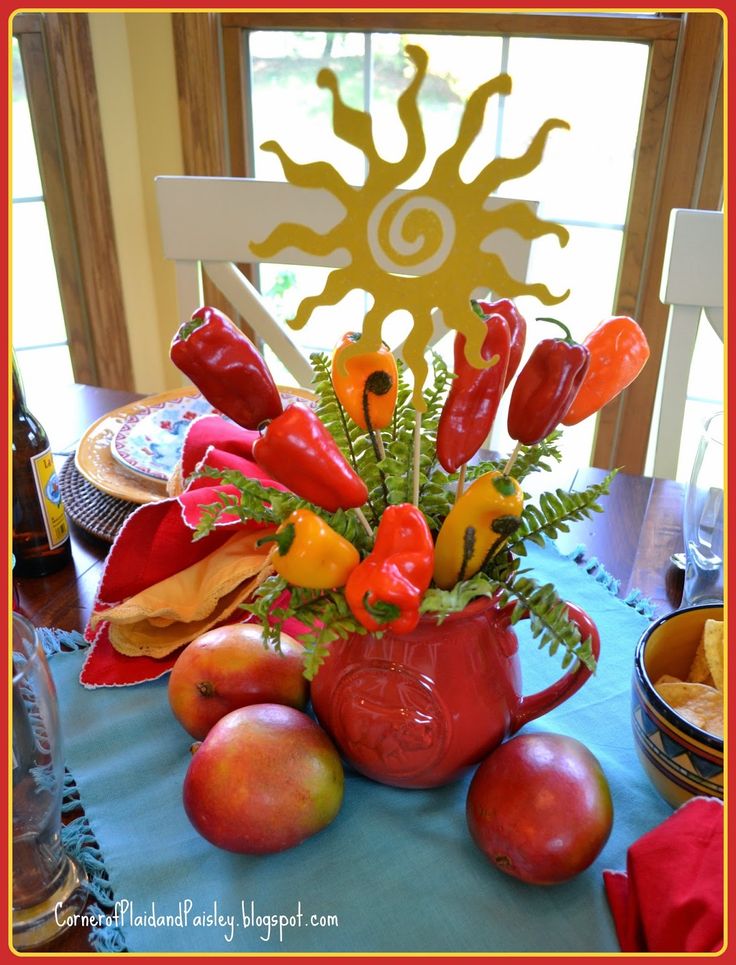 a vase filled with fruit and vegetables sitting on top of a blue tablecloth covered table