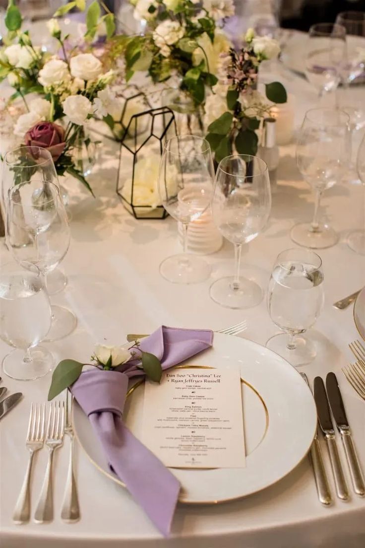 the table is set with silverware and white plates, purple napkins, and floral centerpieces