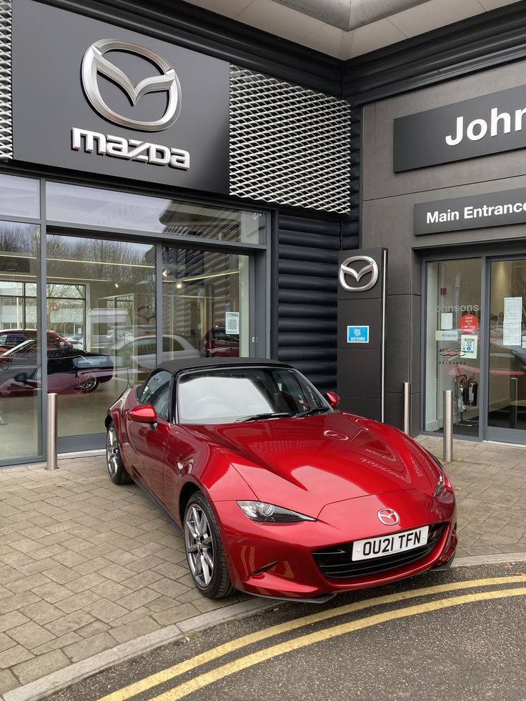 a red sports car parked in front of a mazda dealership