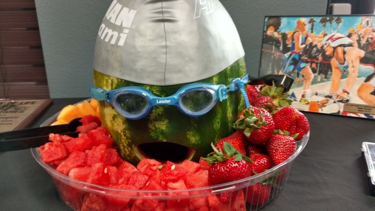 a watermelon sculpture with sunglasses and fruit in front of it