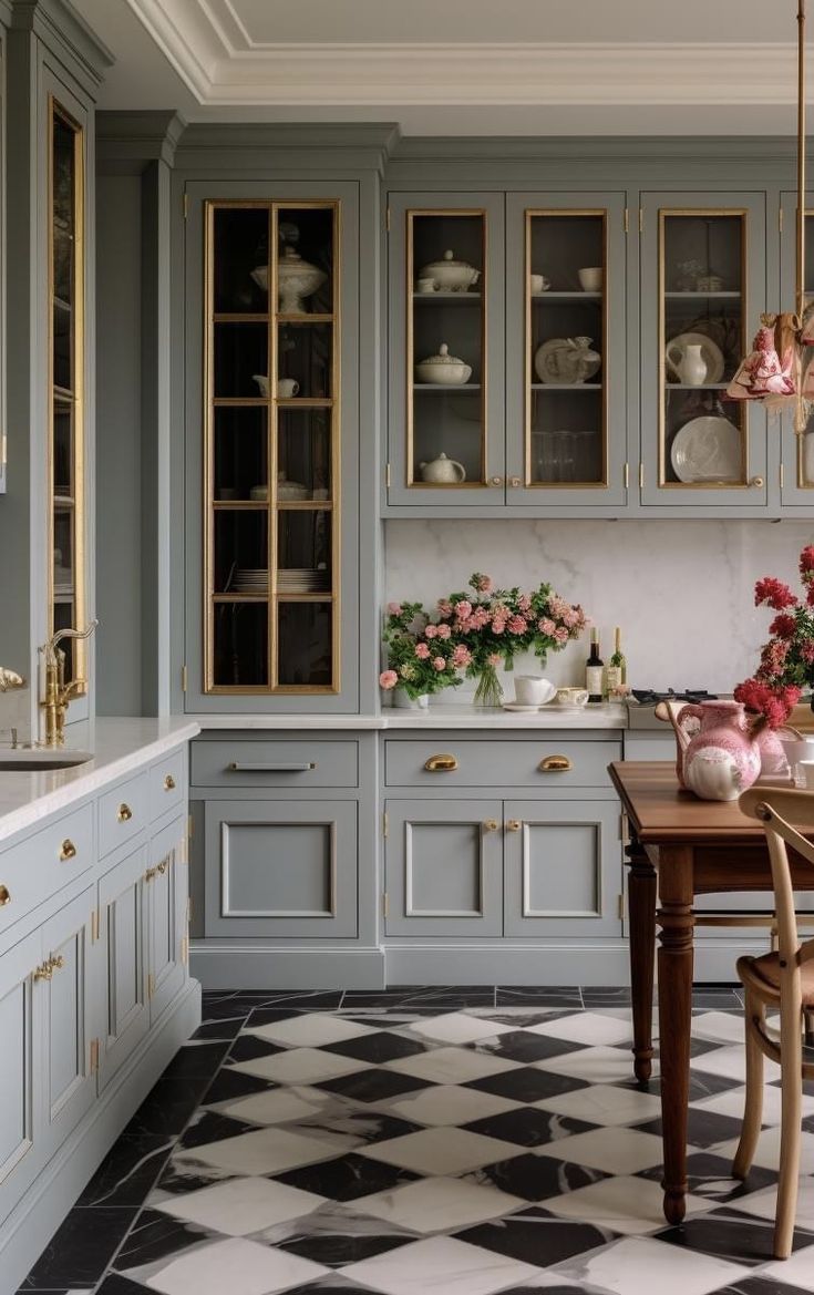 a kitchen with checkered flooring and cabinets in grey tones, pink flowers are on the table