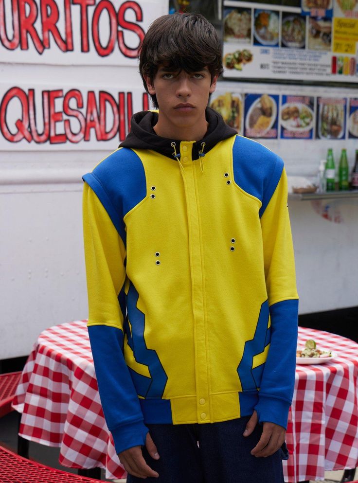 a young boy wearing a yellow and blue jacket standing in front of a food truck