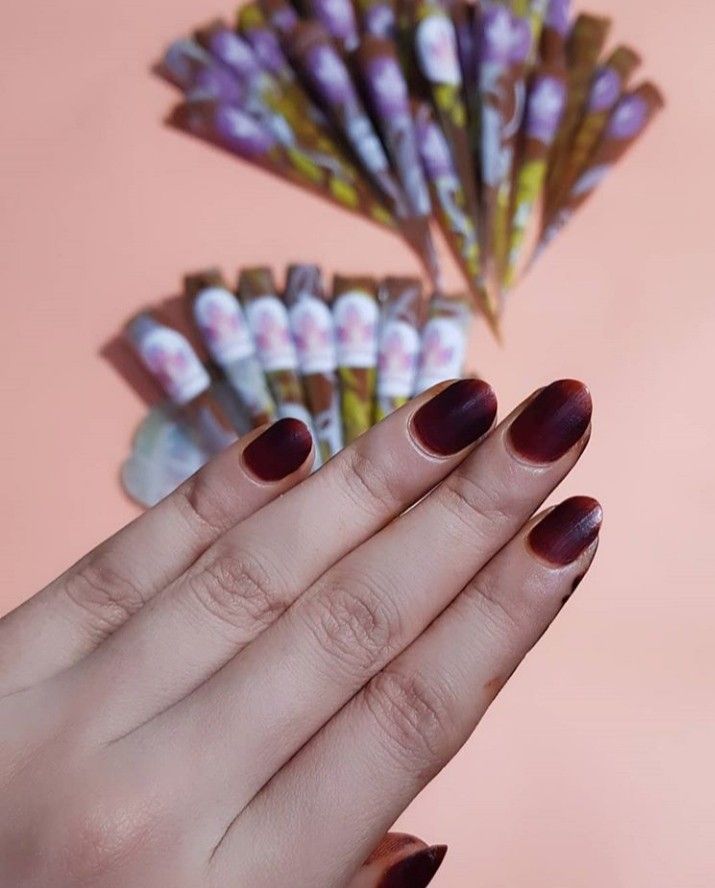 a woman's hand with maroon manicures and some candy sticks in the background