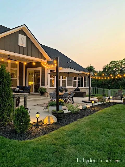 a house with lights on the front porch and landscaping in the back yard at dusk