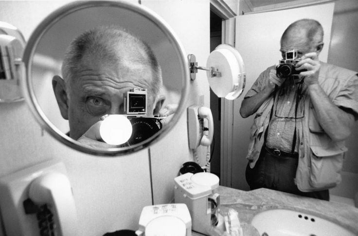 an older man taking a selfie in front of a bathroom mirror with his camera