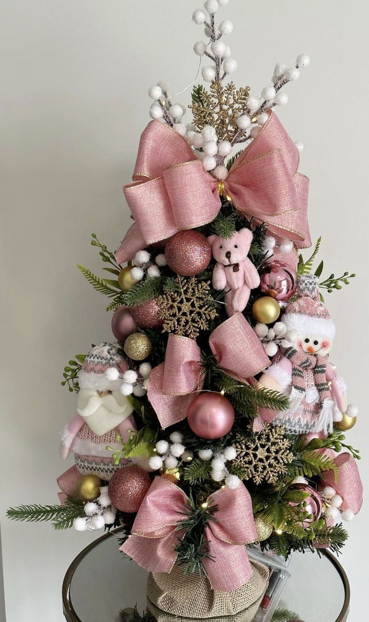 a small christmas tree with pink bows and other decorations on it's top shelf