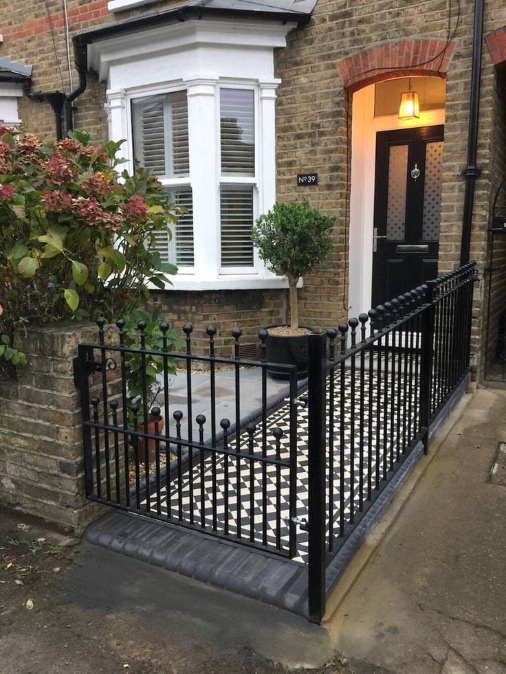 a black iron fence in front of a brick house with potted plants on the doorstep