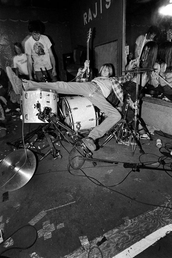 a man laying on top of a drum kit in front of a group of people