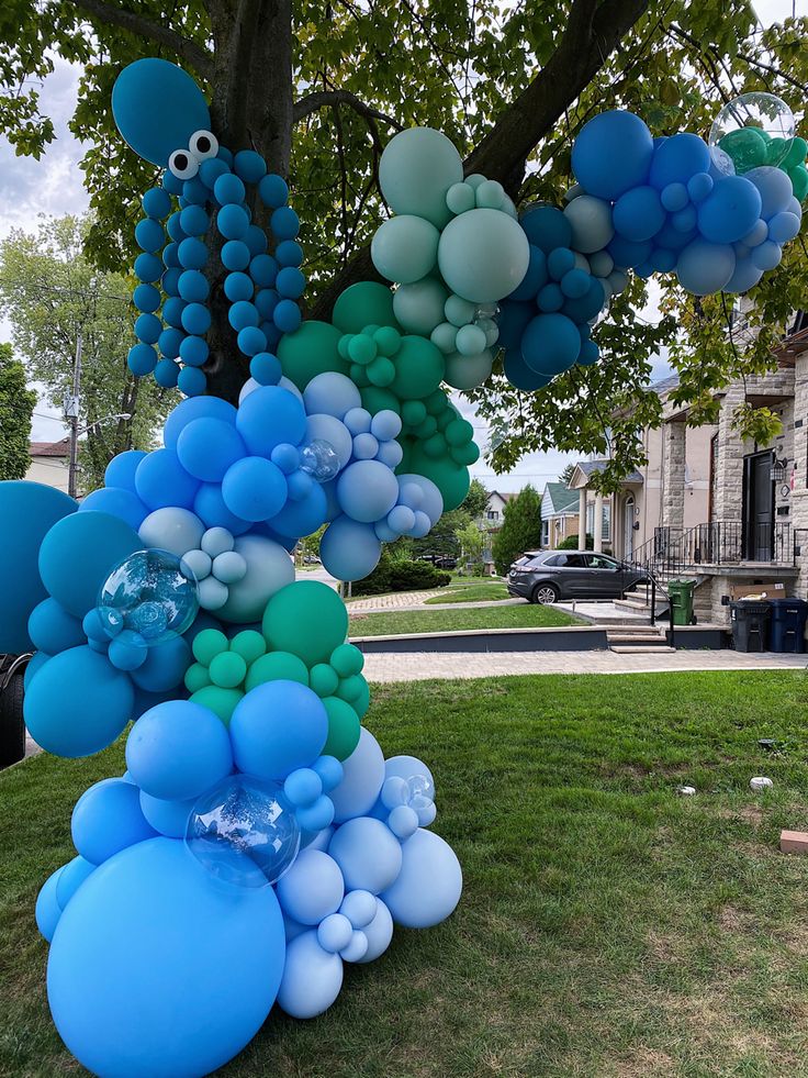 blue and green balloons are hanging from a tree