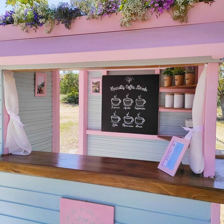 a pink and blue building with flowers growing on the roof, along with a chalkboard sign