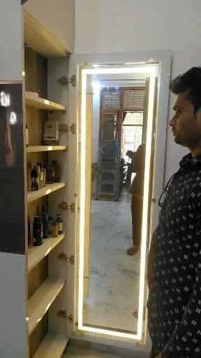 a man standing in front of a large mirror next to shelves with bottles on them