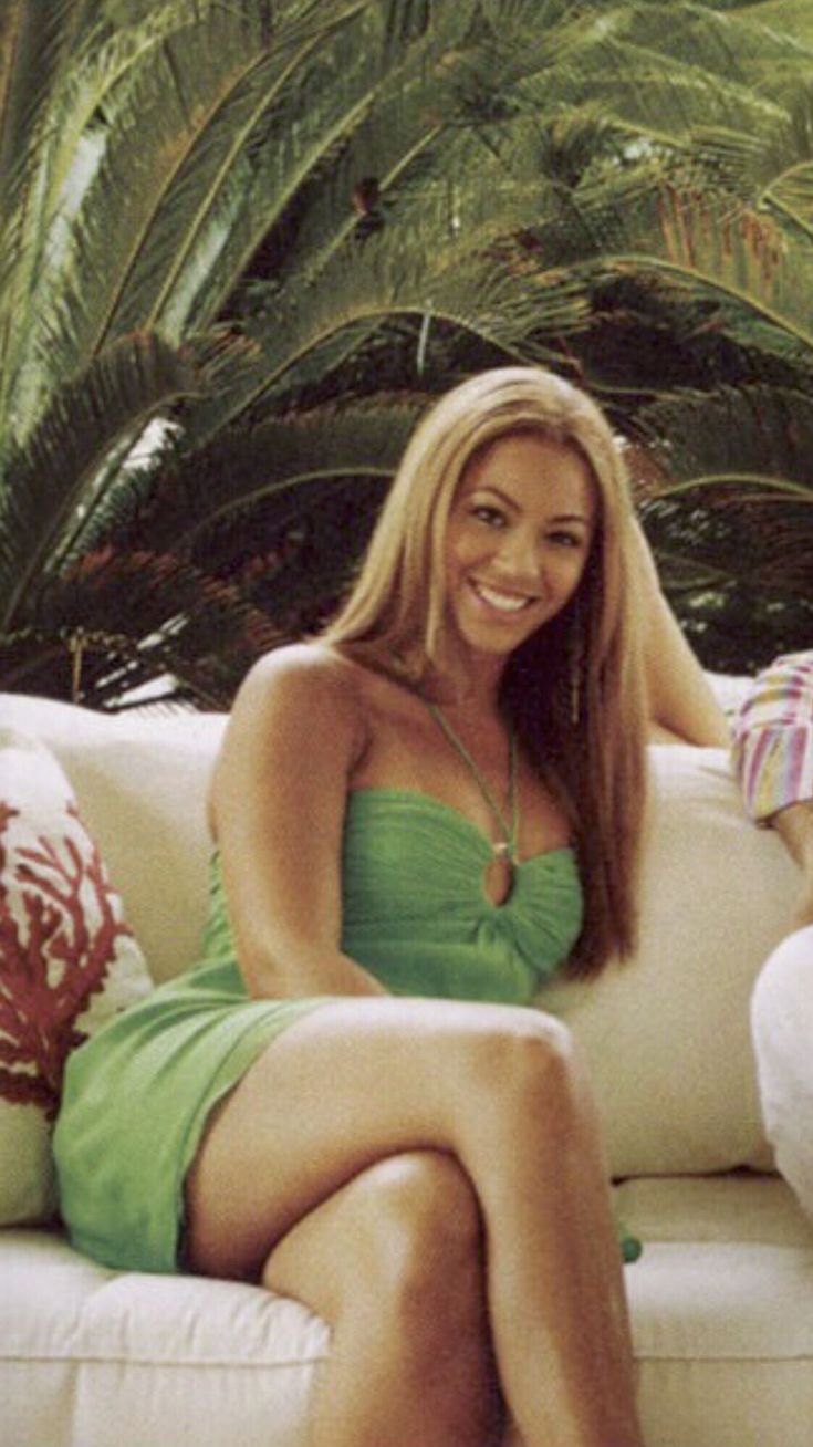 a woman in a green dress sitting on a white couch with palm trees behind her