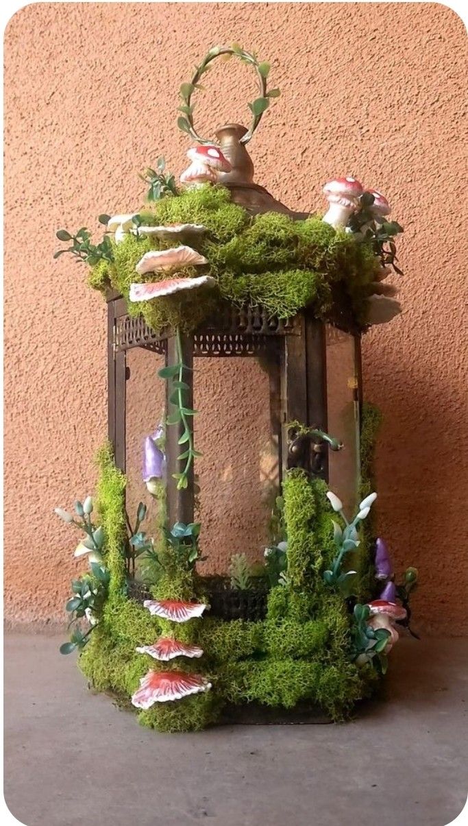 a small lantern with moss growing on it's sides and flowers in the middle