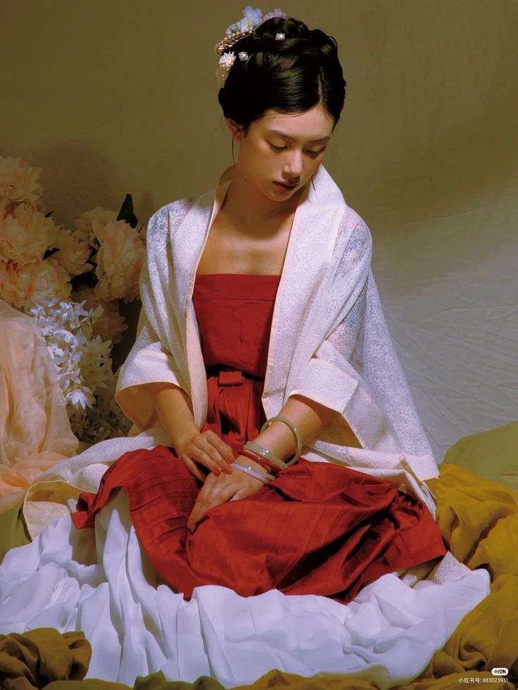 a woman sitting on top of a bed in a red dress and white shawl