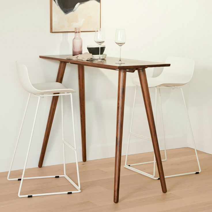 two white chairs and a table with wine glasses on it in front of a painting