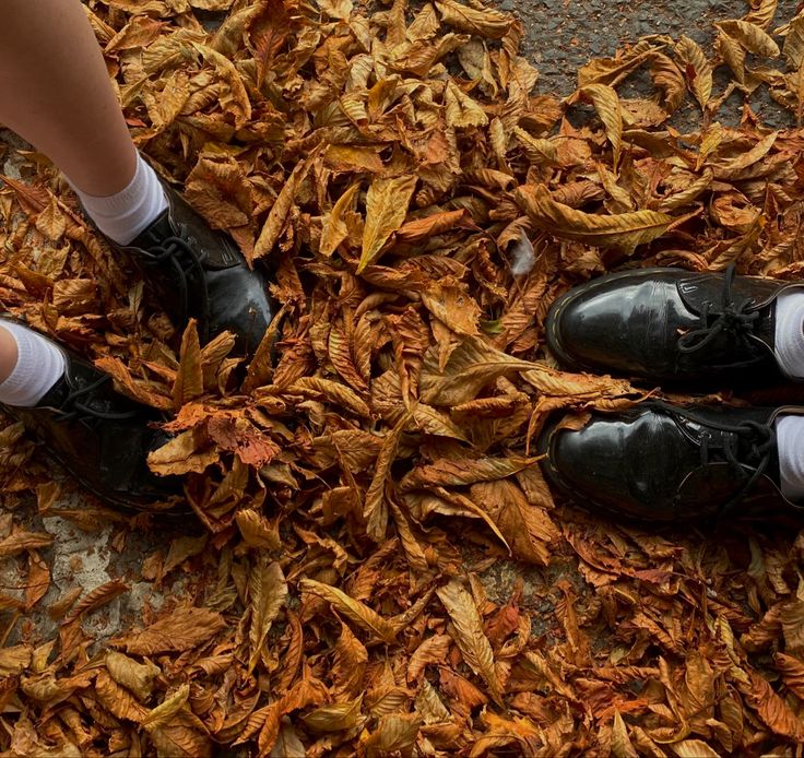 two people in black shoes and white socks are standing on the ground covered with leaves