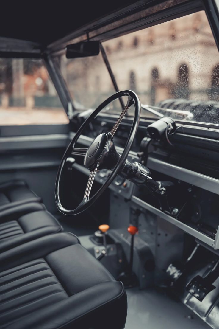 the interior of an old truck with black leather seats and steering wheel, looking out over a city street