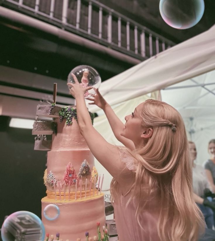 a woman reaching up to grab a bubble from a tall pink cake with lots of candles on it