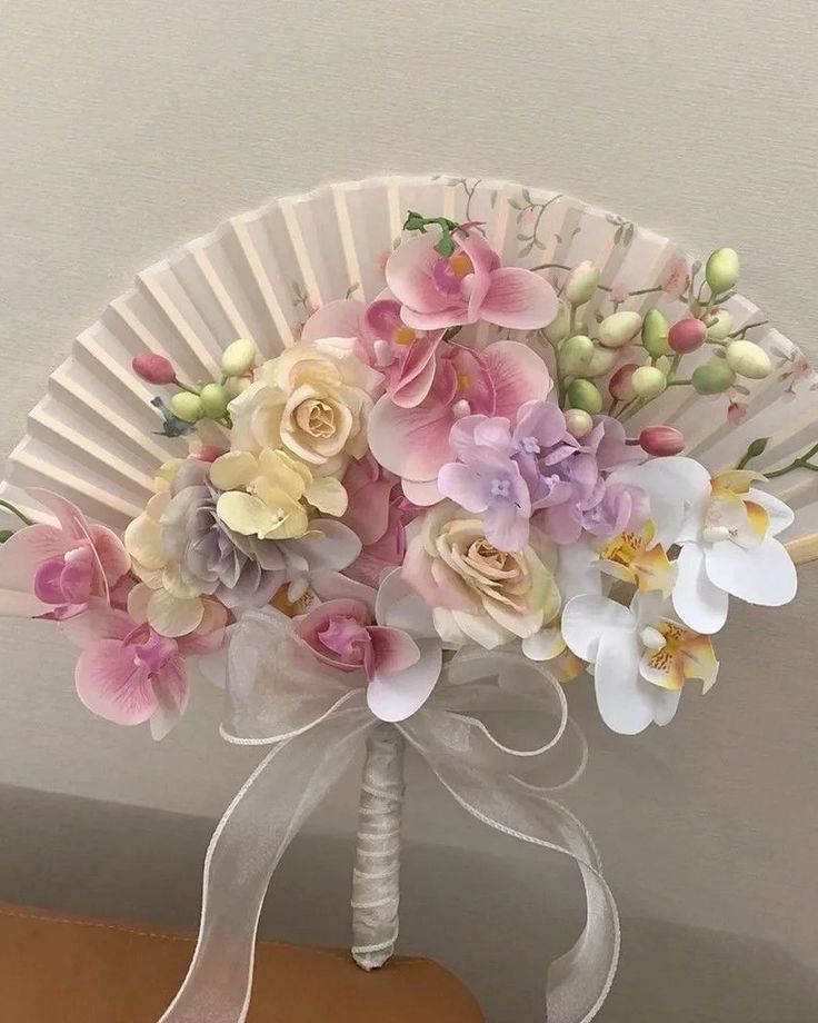 a bouquet of flowers sitting on top of a wooden table next to a white fan