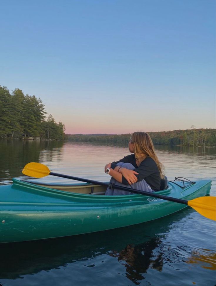 a woman is sitting in a green kayak on the water at sunset or dawn